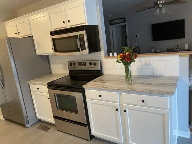 White painted kitchen cabinets with granite countertops, stainless appliances and a gray accent wall