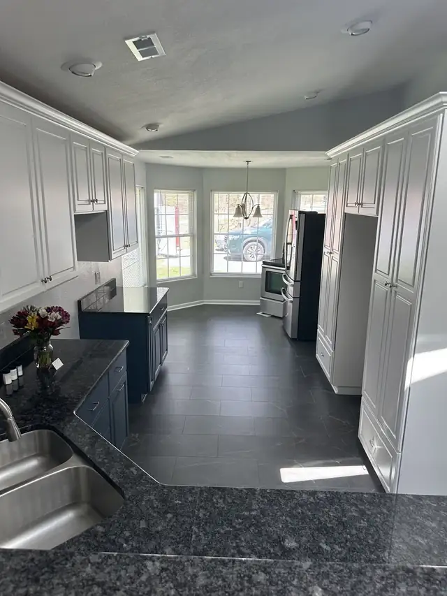 Long kitchen with white tall cabinets, navy lower cabinets, dark granite and a bay window