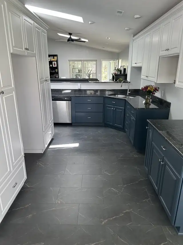 Refinished kitchen with white tall and upper cabinets, navy lower cabinets, dark granite counters and slate-look floor