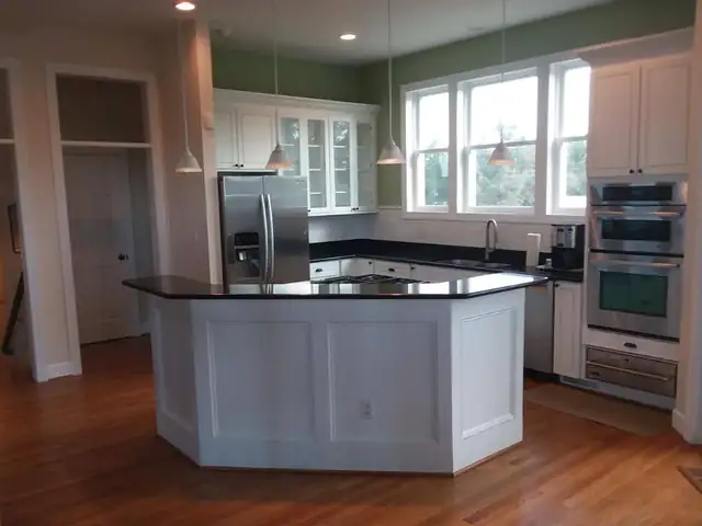 Kitchen with a white angled island, dark countertops, stainless appliances and wood floors