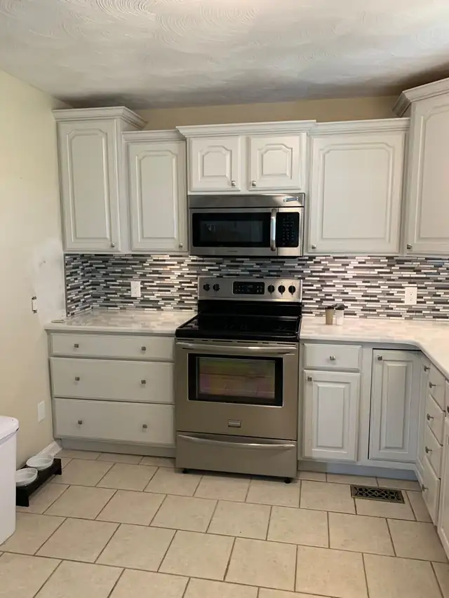 Kitchen cabinets painted white with a gray and white glass mosaic backsplash and stainless range